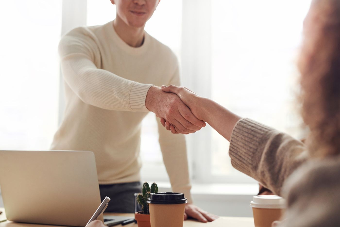 Two people shaking hands across a table at a business meeting