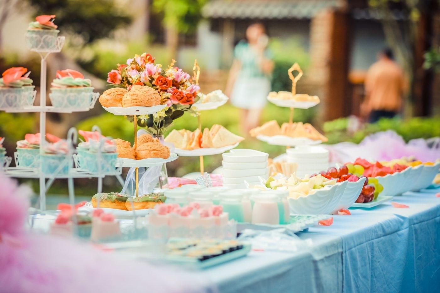 An outdoor celebration table with pastries, flowers and colourful catering displays