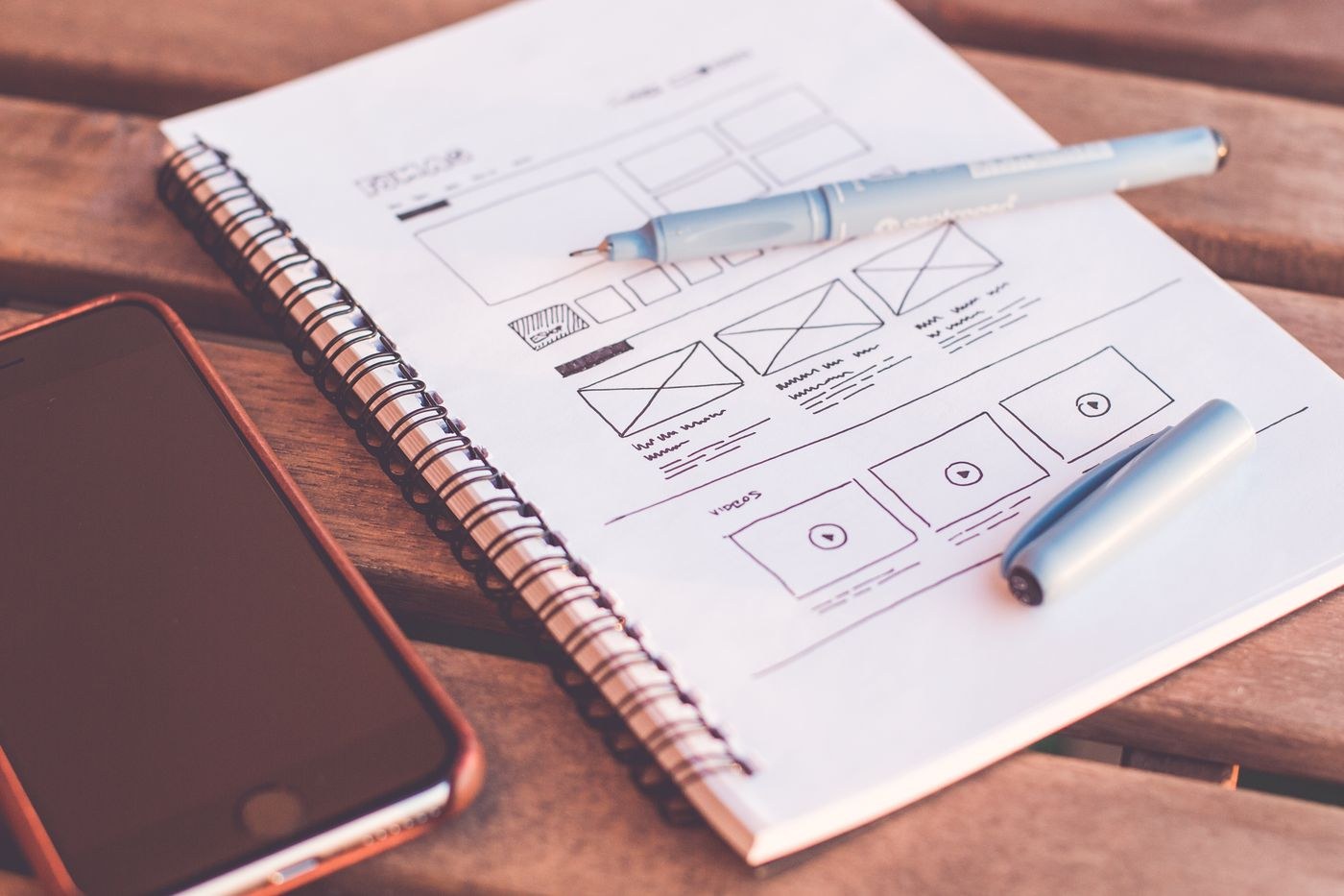 A notebook of website sketches beside a smartphone on a creative workspace